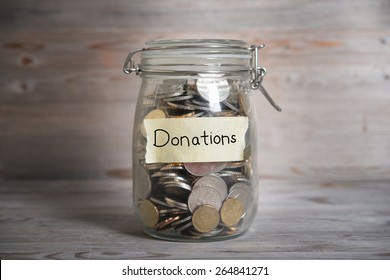 Coins in glass money jar with donations label, financial concept. Vintage wooden background with dramatic light.