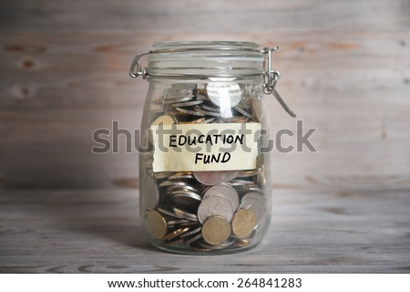 Coins in glass money jar with education fund label, financial concept. Vintage wooden background with dramatic light.