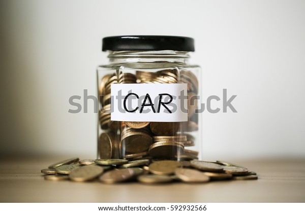 A lot coins in glass money jar on the table.
Saving for car concept.