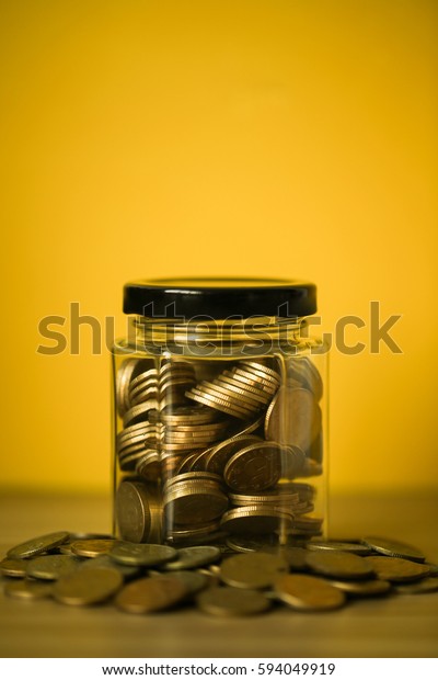 A lot\
coins in glass money jar on yellow\
background.
