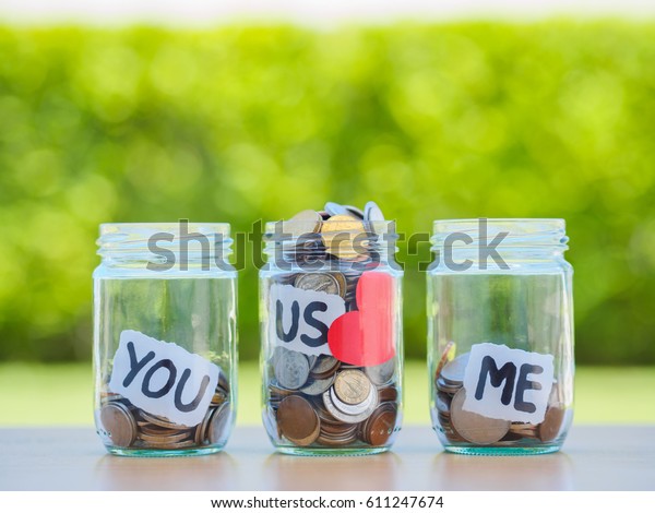 A lot coins in glass money jar on the wood\
table. Saving for family\
concept.