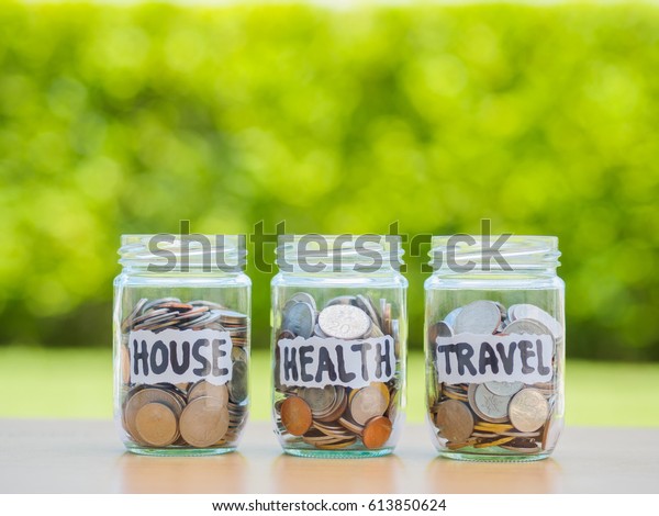 A lot coins in glass money jar
on the wood table. Saving for house, health and travel
concept.