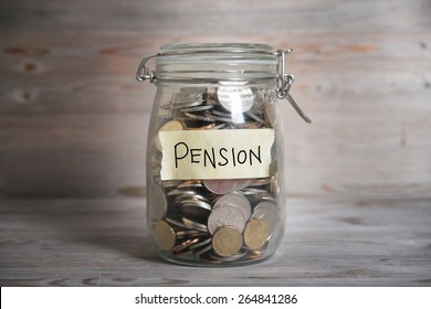 Coins in glass money jar with pension label, financial concept. Vintage wooden background with dramatic light.