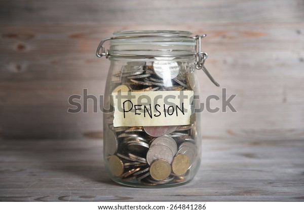 Coins in glass\
money jar with pension label, financial concept. Vintage wooden\
background with dramatic\
light.