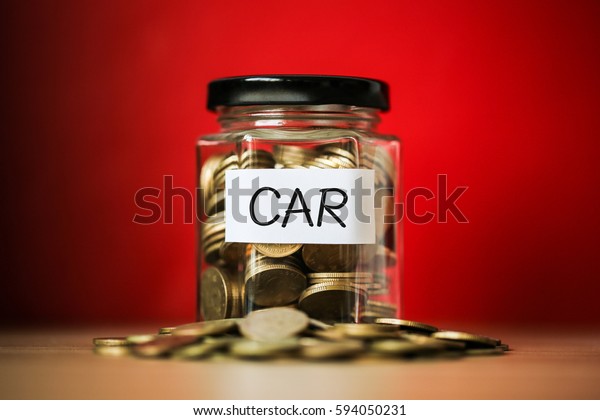 A lot coins in glass money jar with red\
background. Saving for car\
concept.