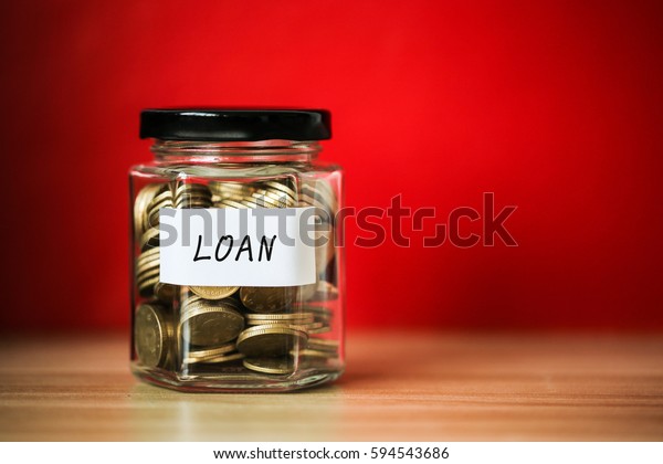 A lot coins in glass money jar with red\
background. Saving for loan\
concept.