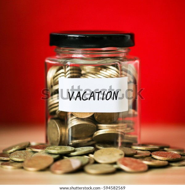 A lot coins in glass money jar with\
red background. Saving for vacation \
concept.