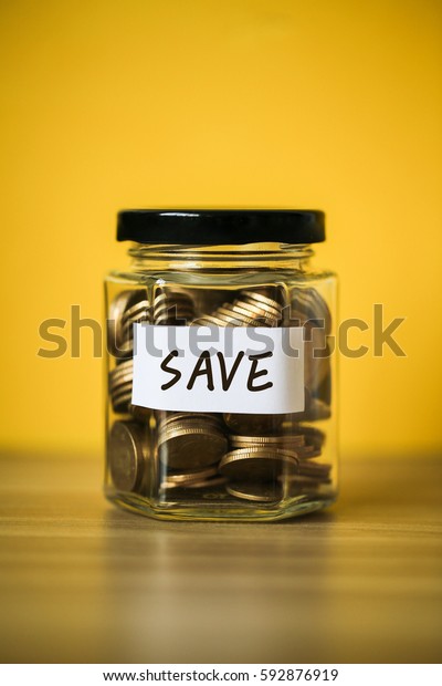 A lot coins in glass money jar with save
money paper on yellow
background.