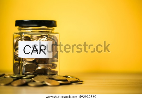 A lot coins in glass money jar with yellow\
background. Saving for car\
concept.
