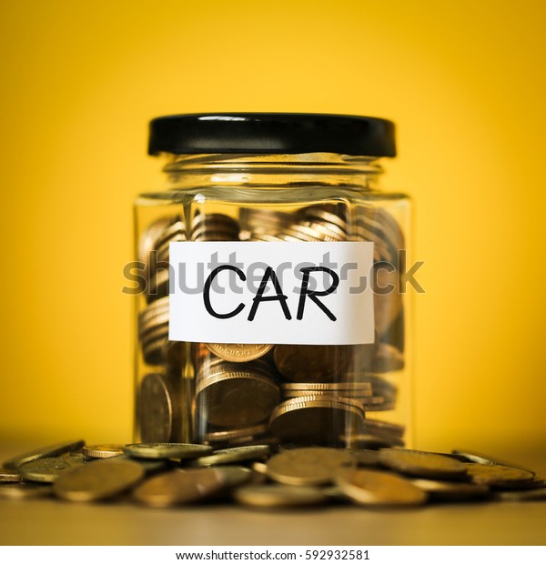 A lot coins in glass money jar with yellow\
background. Saving for car\
concept.