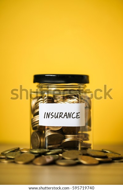 A lot coins in glass money jar with\
yellow background. Saving for Insurance\
concept.