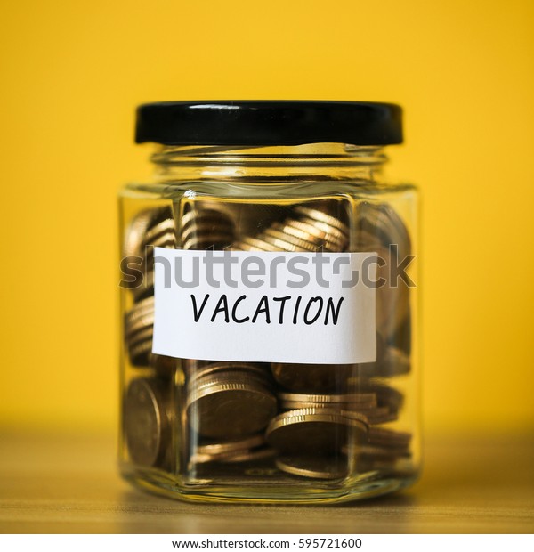 A lot coins in glass money jar with\
yellow background. Saving for vacation\
concept.