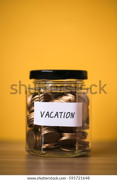 A lot coins in glass money jar with\
yellow background. Saving for vacation\
concept.