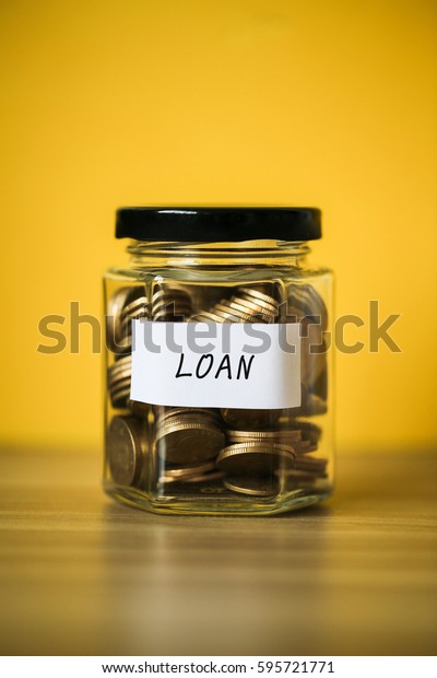 A lot coins in glass money jar with yellow\
background. Saving for loan\
concept.