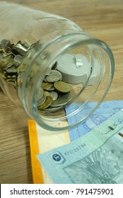 Coins Inside A Cookie Jar And Paper Money  Infront Of Mouth Of Cookie Jar In Wood Background