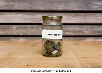 Coins in a jar with label written Investment on wooden background. Financial concept.