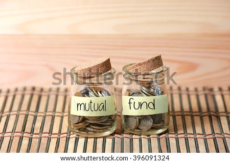Coins in jar. Writing Mutual Fund on two jar with wooden pallet background. Selective focus with shallow depth of field.