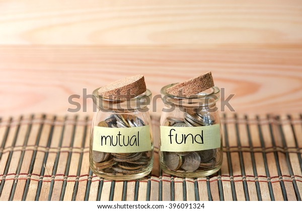 Coins in jar. Writing Mutual Fund on two jar with\
wooden pallet background. Selective focus with shallow depth of\
field.