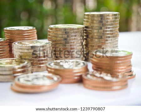 coins money stack on white tabletop with natural green background, savings or investing concept