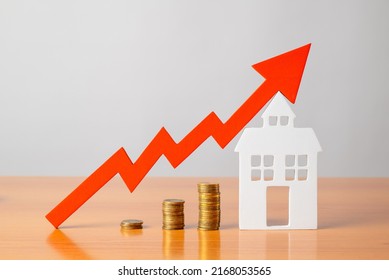 Coins On A Table, A Red Up Arrow And House. The Concept Of The Rising Price Of Real Estate