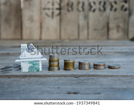 Coins in stacks in descending order and origami house from a banknote of 100 dollars on a blackboard. Long-term home mortgage. Tax and mortgage holidays. Old boards in the background Foto stock © 