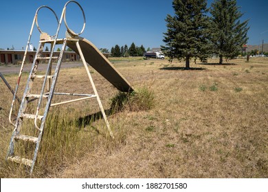 Cokeville, Wyoming - August 6, 2020: Swingset And Playground At An Old Abandoned Seedy Motel, With Overgrown Weeds In The Parking Lot