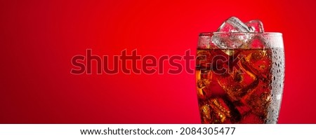 Cola beverage with ice. Fresh cold sweet drink with ice cubes. Over red background with copy space