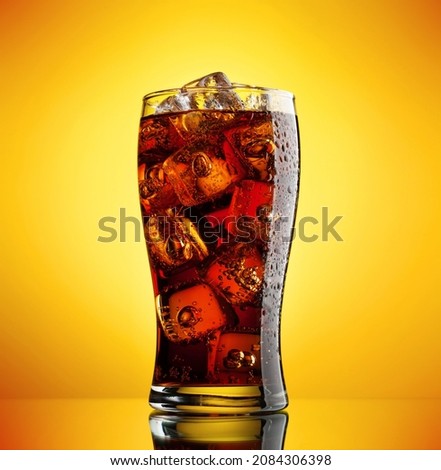 Cola with ice. Fresh cold sweet drink with ice cubes. Over yellow background