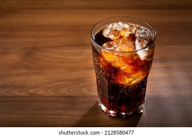 Cola soda glass with ice cubes on wooden table.
