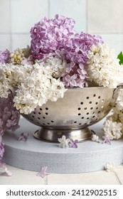 Colander with Beautiful fragrant lilac flowers near white tile