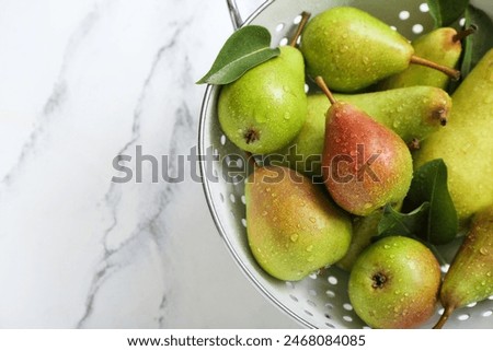 Colander with ripe pears on white marble table, closeup
