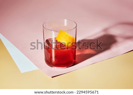 Cold alcoholic or non-alcoholic cocktail with big ice cube and orange. Hard light, deep shadow.