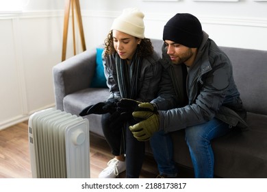 Cold Attractive Woman And Man Sitting On The Sofa And Trying To Stay Warm During A Bleak Winter With A Heater 