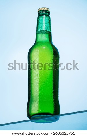 A cold beer bottle standing on a glass table against a vibrant blue background