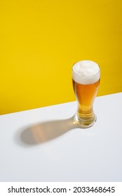 Cold beer served in a glass with white foam on a white table and yellow background, no people