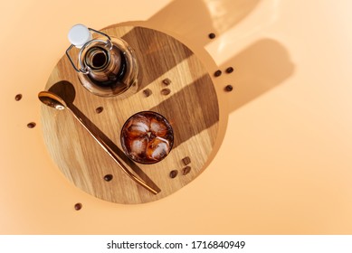 Cold brew coffee with ice cubes in glass and cofee beans on wooden tray,beige background,hard light,top view