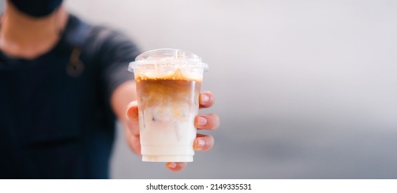 Cold brewed iced latte coffee, Ice coffee latte cup in a plastic glass on. barista hand in coffee cafe.banner background.Cold brew coffee ads.Latte with milk caffeine.plastic ice cup.Arabica roasted. - Shutterstock ID 2149335531