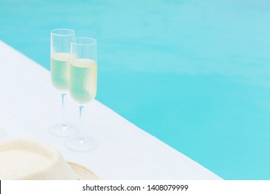 Cold Champagne Bottle In Ice Bucket And Two Glasses Of Sparkling Wine On Rattan Table Near Infinity Swimming Pool