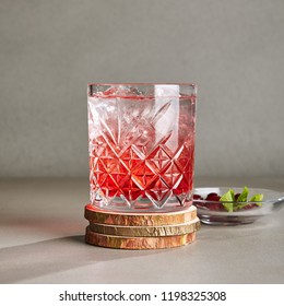 Cold Clear Drink Of Red Berries With Ice, Water, Sugar In A Crystal Glass On Wooden Plate. Refreshment Cranberry Iced Tea, Beverage, Cocktail, Punch, Lemonade, Fruit Drink Or Compote Close Up