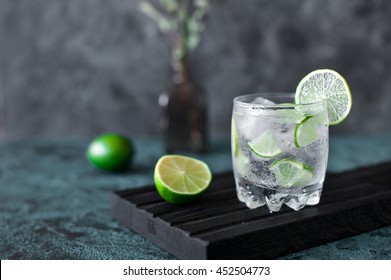 Cold cocktail with lime, tonic, vodka and ice on dark background