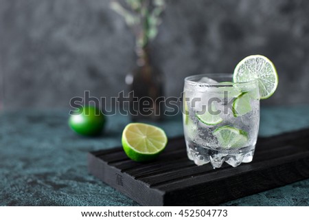 Cold cocktail with lime, tonic, vodka and ice on dark background