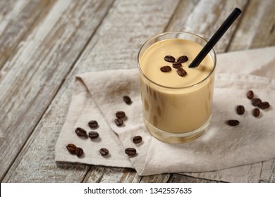 Cold coffee cream milkshake smoothie drink in a glass topped with coffee beans on a wooden rustic table with copy space.