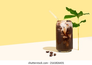 Cold coffee drink, coffee beans and leaves on a yellow isometric diagonal projection background. Can-shaped glass cup of coffee with plant-based milk. Concept of sustainable summer drinks. Creative. - Powered by Shutterstock