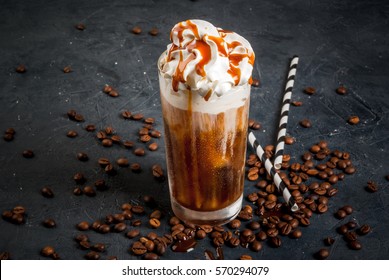 Cold coffee drink frappe (frappuccino), with whipped cream and caramel syrup, with straws and grains of coffee on a dark gray stone table, copy space 