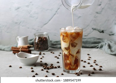 Cold Coffee In A Tall Glass With Cream Being Poured Into It Showing The Texture Of The Drink. Light Gray Background.
