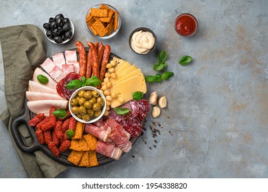 Cold cuts, cheese, olives, crackers, basil and sauces on a gray background with space to copy. Top view, horizontal.