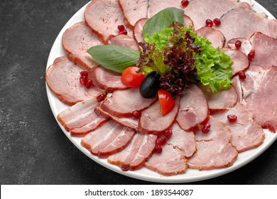 Cold cuts thinly sliced, sausage, bacon, boiled pork, meat, with lettuce, basil, cherry tomatoes and pomegranate seeds, on a white plate