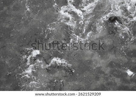 A cold, dark-toned river flows steadily with snow-covered riverbanks on each side, reflecting the dim sky and adding a quiet, somber mood to the wintry natural scene.