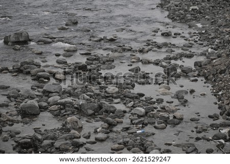 A cold, dark-toned river flows steadily with snow-covered riverbanks on each side, reflecting the dim sky and adding a quiet, somber mood to the wintry natural scene.