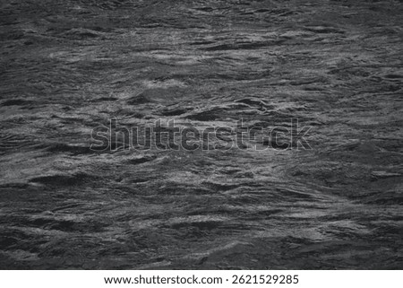 A cold, dark-toned river flows steadily with snow-covered riverbanks on each side, reflecting the dim sky and adding a quiet, somber mood to the wintry natural scene.
